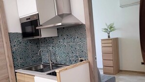 A compact kitchen with a built-in oven, microwave, and stainless steel range hood. - Room 102 -- studio apartment. (Pompei)