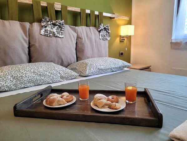A hotel room with a bed, pillows, a tray with croissants and juice, and a nightstand with a lamp.