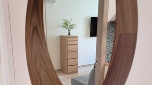 A mirror with a wooden frame reflecting a room with a wooden dresser, a small plant, and a television on the wall. - Room 102 -- studio apartment. (Pompei)