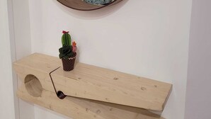 A round mirror on a wall with a wooden shelf below it, holding a small cactus and a pair of sunglasses. - Room 102 -- studio apartment. (Pompei)