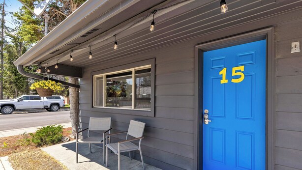 A building with a blue door marked with the number 15, a small window, and two chairs outside. - Cozy Lazy Duck Inn #15 features a King bed and kitchenette, just 1 min from Yellowstone. (West Yellowstone)