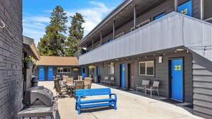 A motel with outdoor seating, a barbecue grill, and a blue bench. - Cozy Lazy Duck Inn #15 features a King bed and kitchenette, just 1 min from Yellowstone. (West Yellowstone)