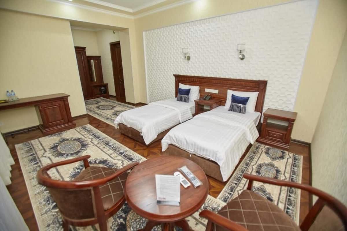 A hotel room with two beds, a wooden nightstand, a small table, and a chair.
