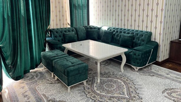 Ein smaragdgrünes, modulartes Sofa mit Samtbezug, ein weißer Couchtisch, ein gemustertes Teppich und gestreifte Tapete.