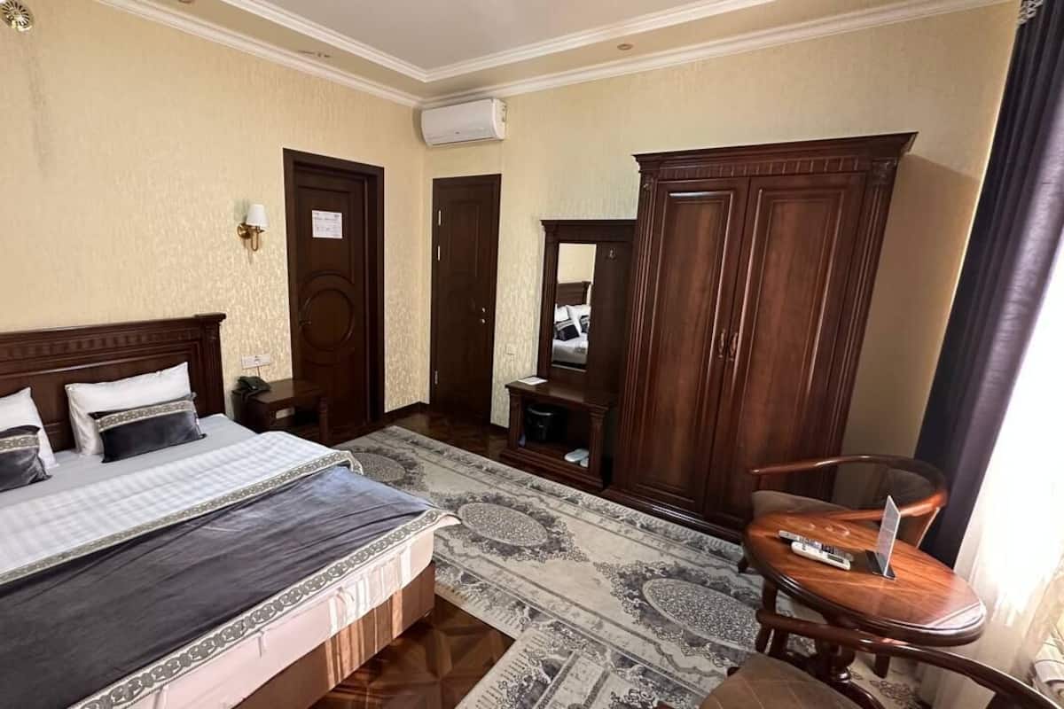 A hotel room with a large bed, a wooden wardrobe, a desk with a chair, and a carpeted floor.