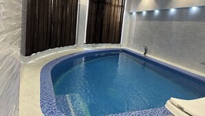 Ein Innenpool mit Fliesenrand, dunklen Vorhängen und einer Deckenleuchte.
