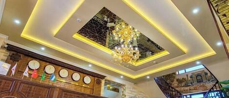 Un hall de hotel con mostrador de recepción, una araña de cristal, una escalera y un suelo estampado.