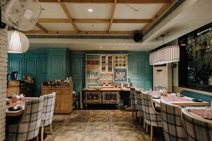 Un comedor acogedor con mesas y sillas de madera, una isla central con una estufa antigua y paredes color turquesa.
