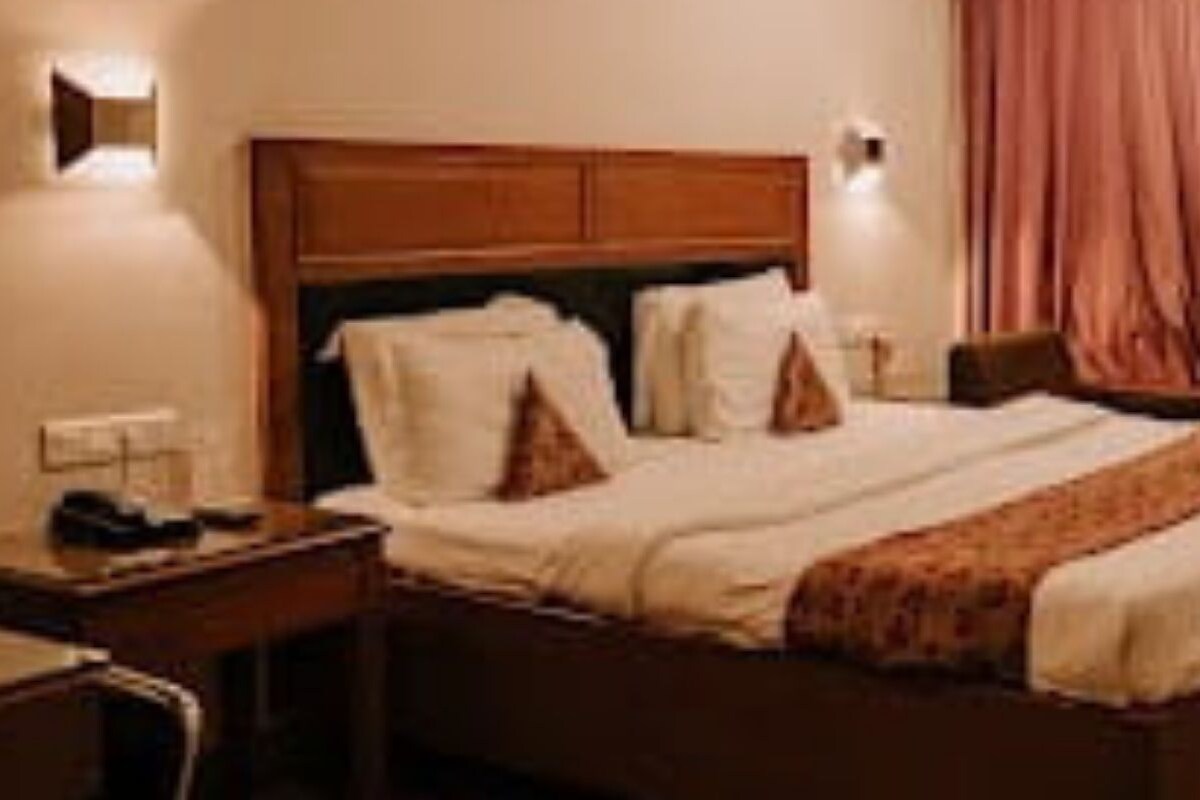 Una habitación de hotel con una cama, una mesita de noche, una lámpara y un ventanal con cortinas.