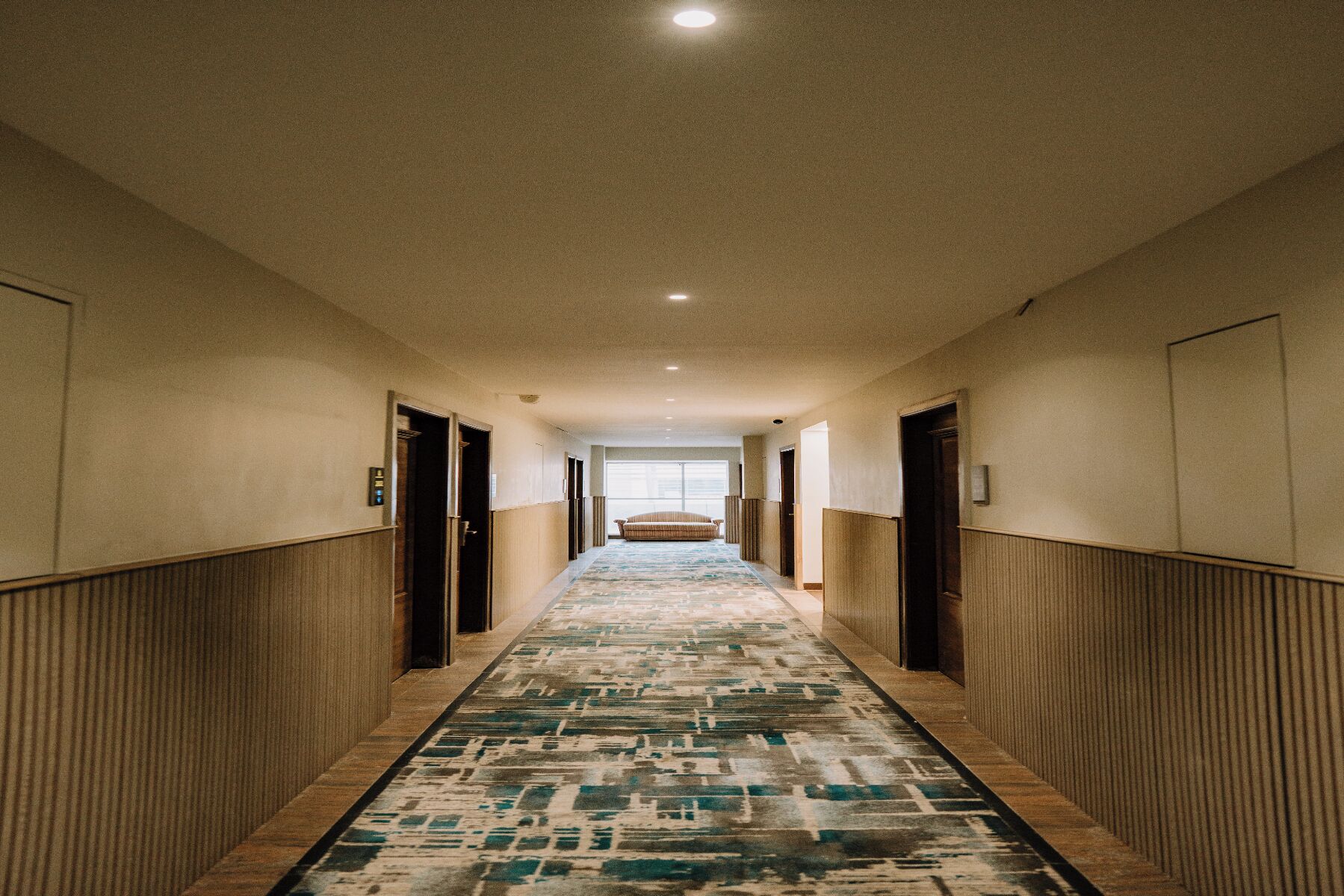 A hotel hallway with a patterned carpet, wooden paneling, and doors leading to rooms.