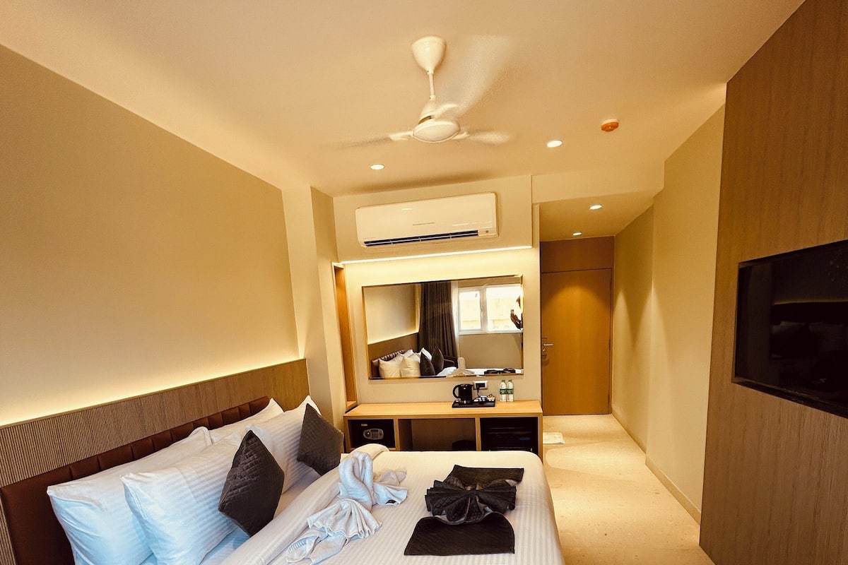 A modern hotel room with a large bed, a bedside table, a mirror, and a TV mounted on the wall.