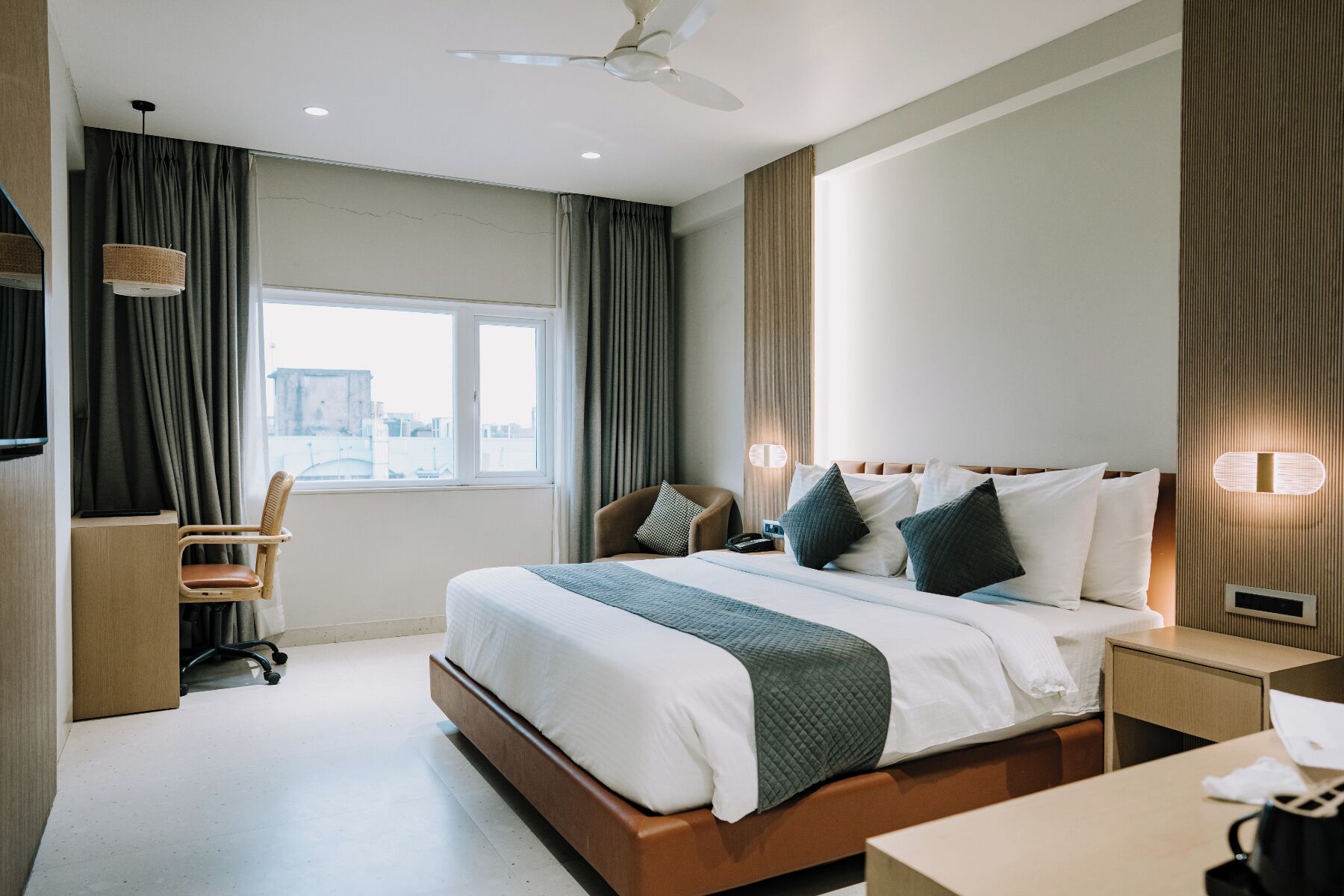 Habitación de hotel con cama, mesita de noche, silla, escritorio y ventana con cortinas.