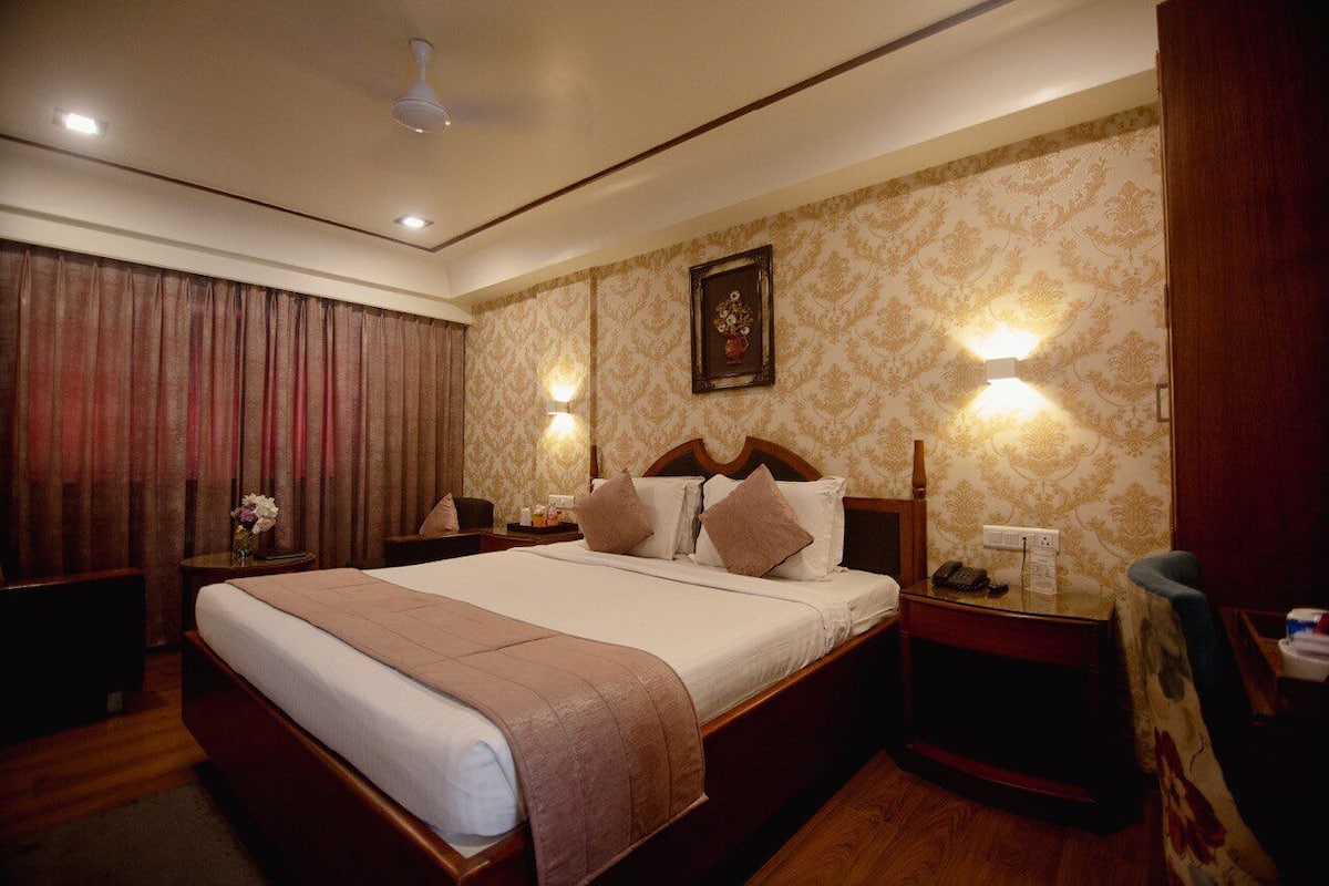 A hotel room with a large bed, two bedside tables, a nightstand, a ceiling fan, and a wall-mounted light fixture.