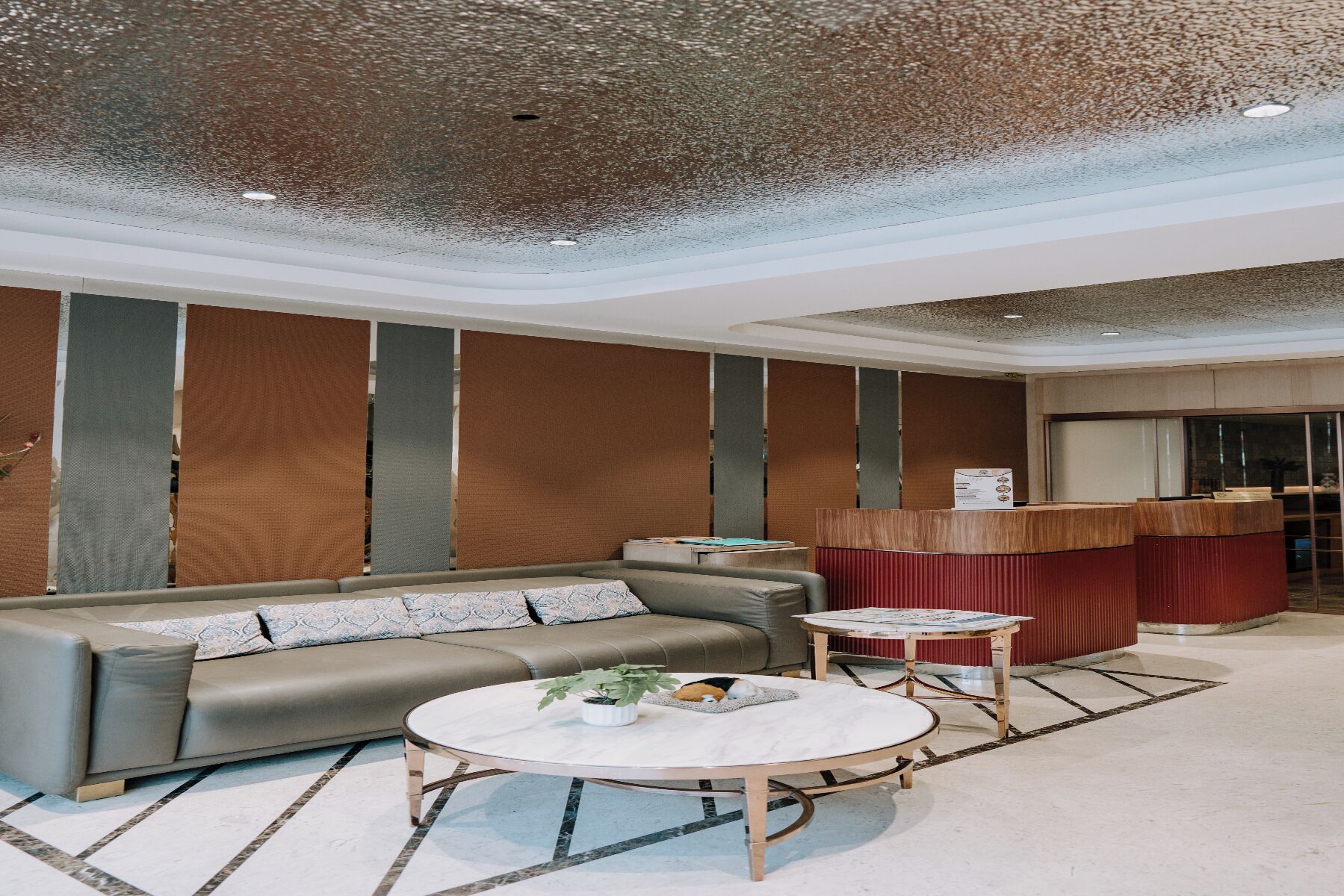 En modern hotellobby med en soffa, ett runt soffbord och en röd accentvägg.