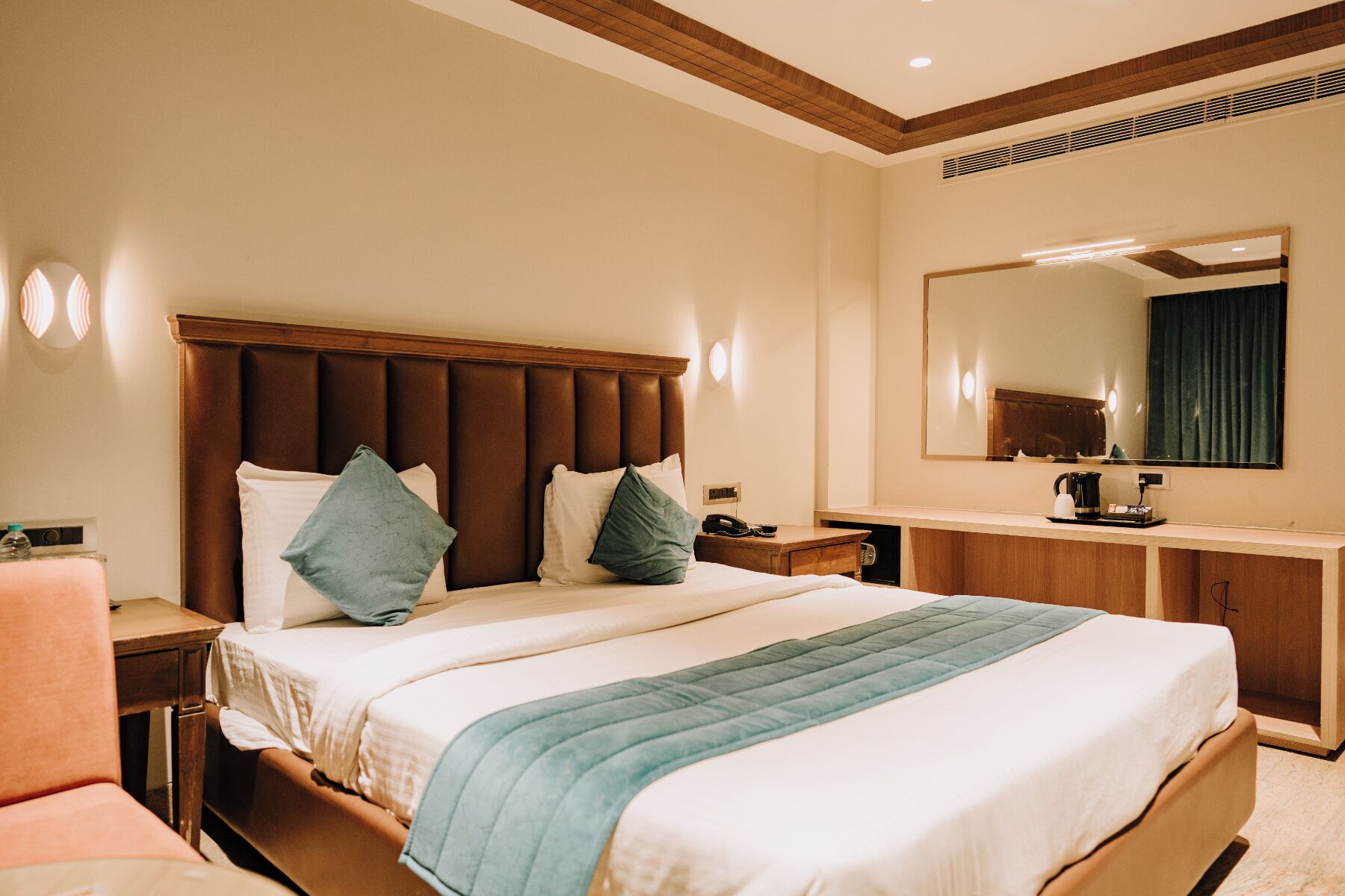 Una habitación de hotel con una cama grande, una mesita de noche, un espejo y una cafetera.
