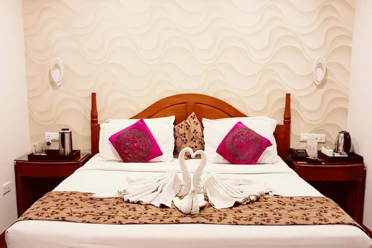 A hotel room with a bed, two nightstands, a decorative wall, and a swan towel arrangement.