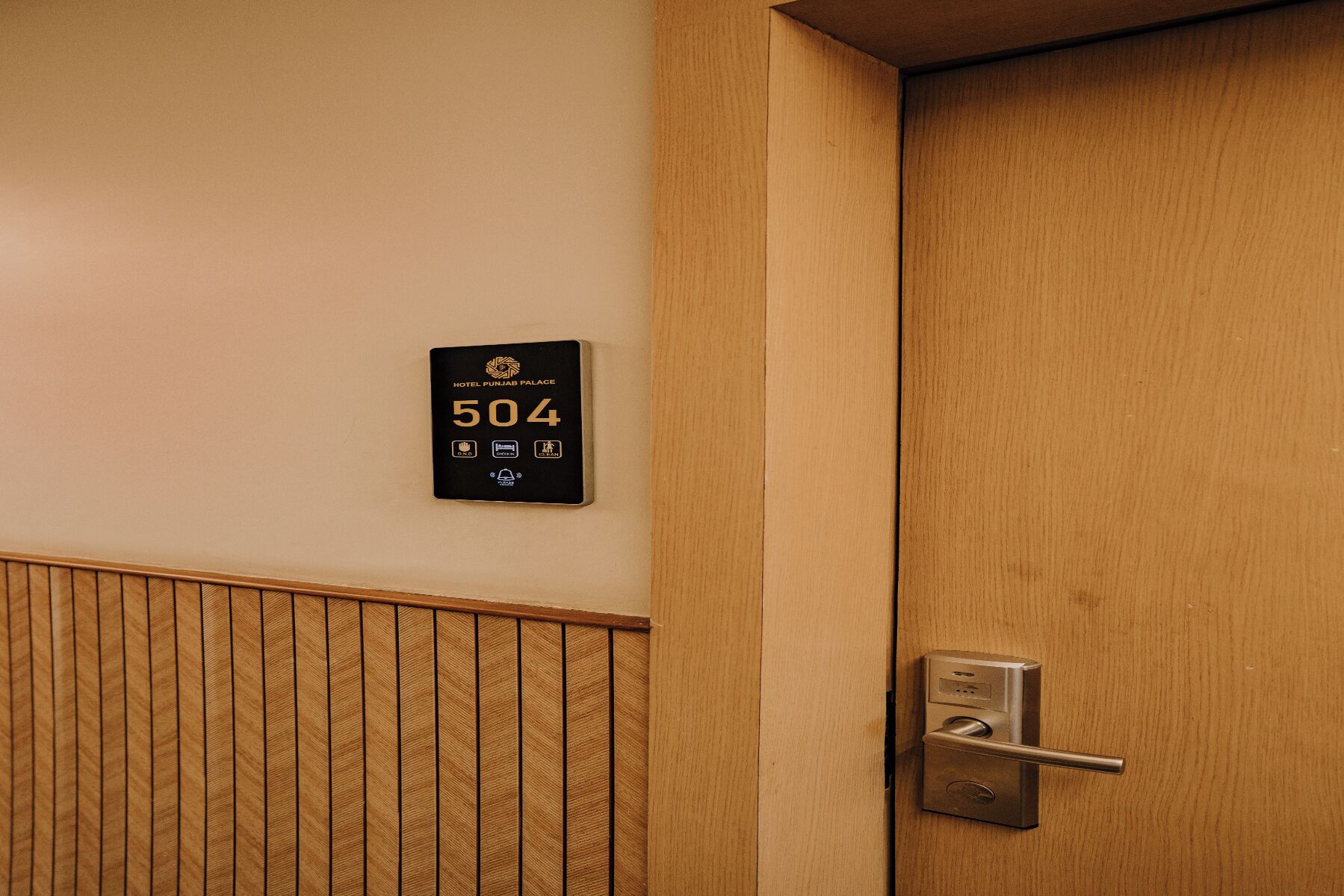 A hotel room door with a number plate indicating room 504, a modern door handle, and a wooden panel design on the wall.