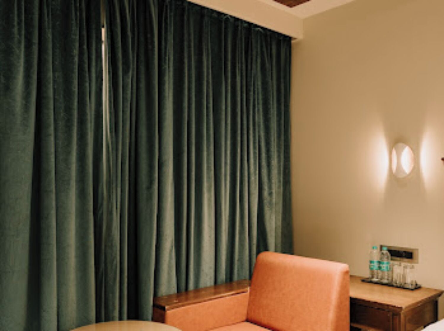 A hotel room with a bed, a wooden nightstand, a chair, and a curtain.