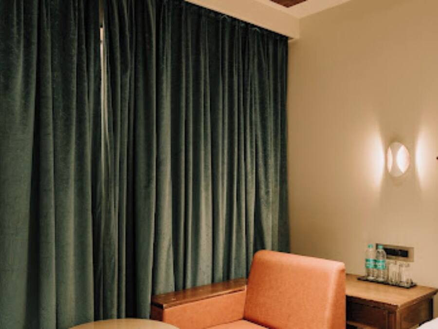 A hotel room with a bed, a wooden nightstand, a chair, and a curtain.