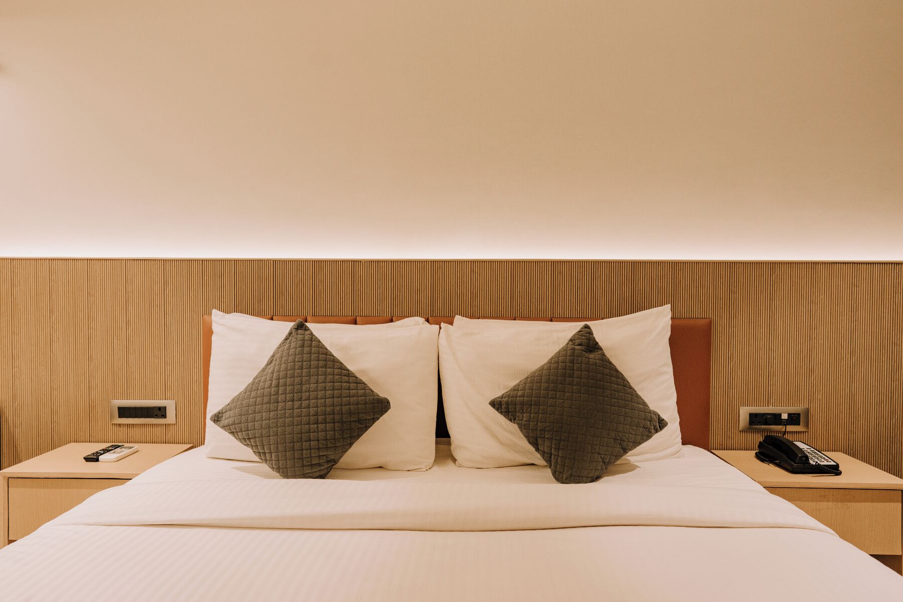 A hotel room with a bed, two bedside tables, and a wooden headboard.