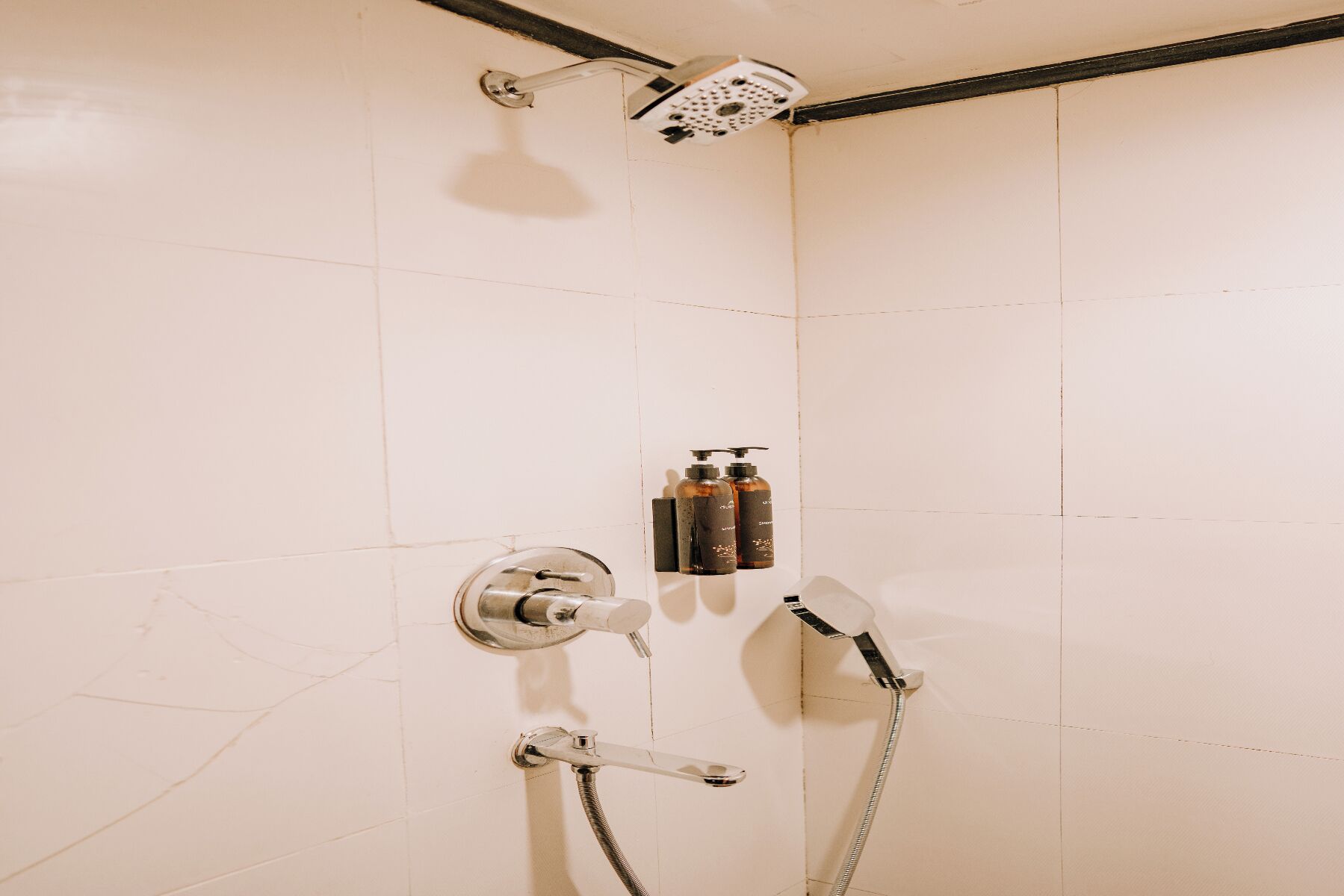 Une douche équipée d’un pommeau de douche à main, d’un robinet mural et de deux bouteilles de shampoing.