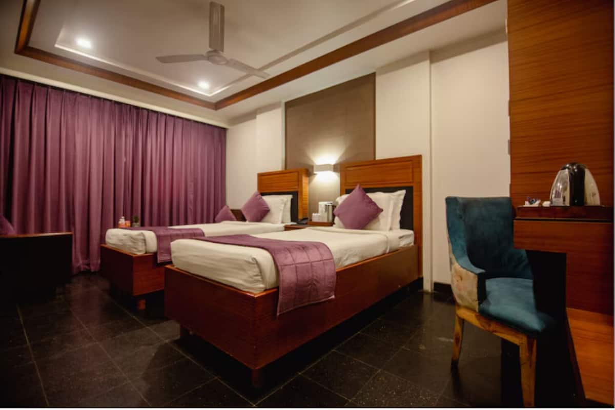 A hotel room with two beds, a desk, a chair, a ceiling fan, and a nightstand with a lamp.
