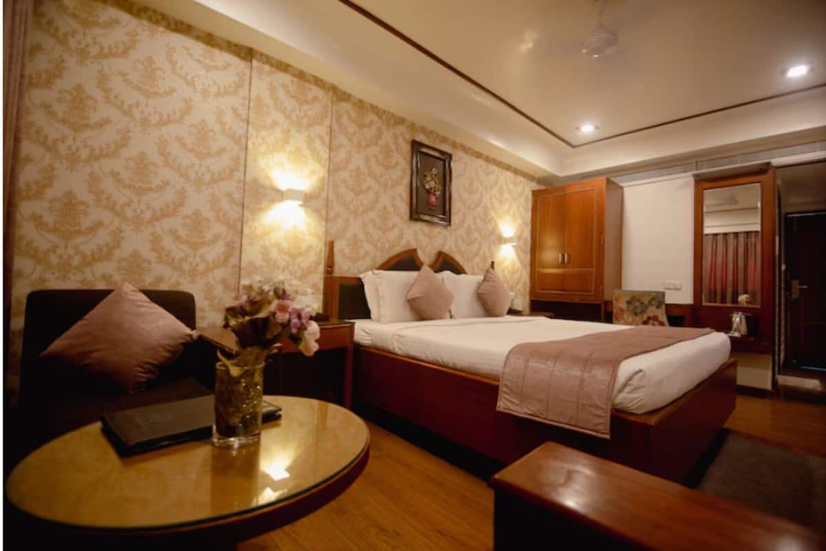 A hotel room with a large bed, a bedside table with a vase of flowers, a wooden nightstand, and a wardrobe.