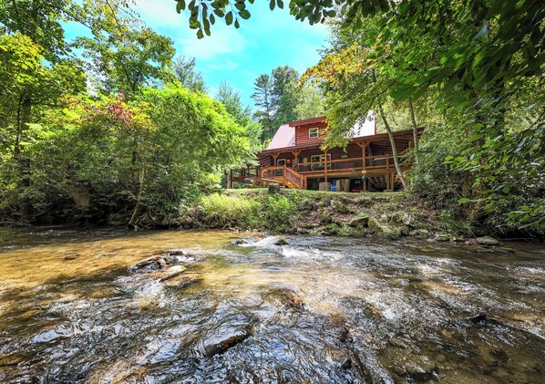 A cabin with a wooden deck overlooking a river.