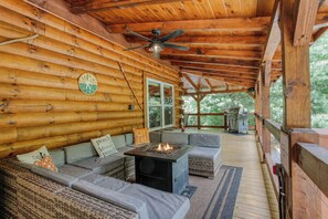 A log cabin with a covered porch, a fireplace, and a ceiling fan.