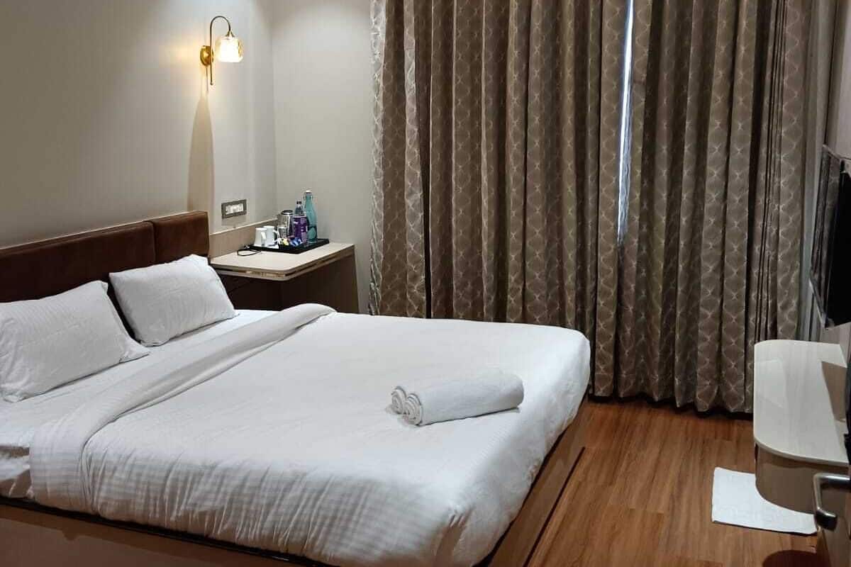 Une chambre d’hôtel équipée d’un lit, d’une table de chevet, d’une lampe, de rideaux et d’un ventilateur de plafond.