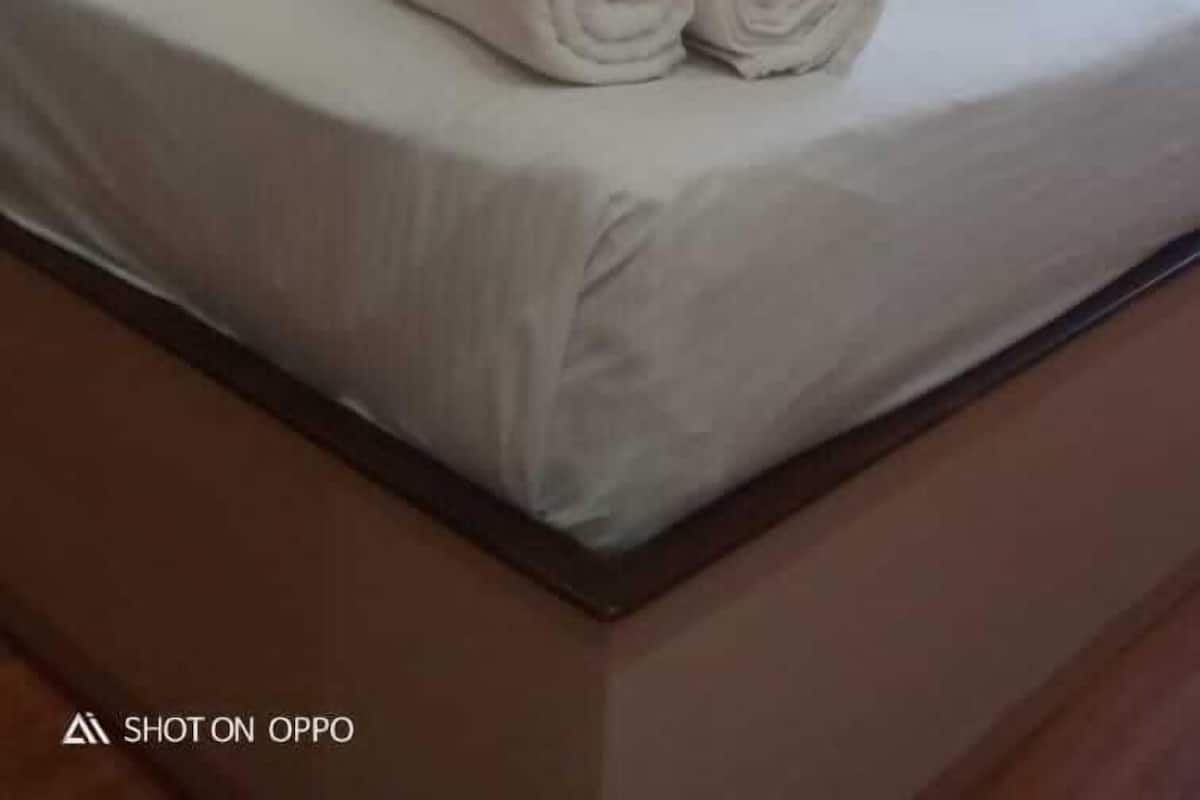 Une chambre d’hôtel avec un lit bien fait, une lampe fixée au mur et une fenêtre avec des stores.