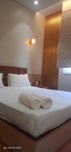 Een hotelkamer met een netjes opgemaakt bed, een wandlamp en een raam met zonwering.