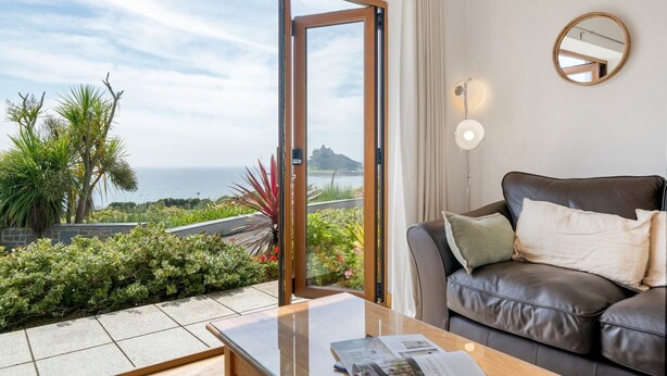 Una sala de estar moderna con un sofá de cuero, una mesa de centro de vidrio y vistas al océano y la vegetación.