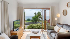 Una sala de estar con un televisor grande, un sofá de cuero, una mesa de centro y vistas al mar a través de puertas abiertas.