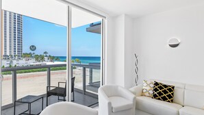 Un salón moderno con un sofá blanco, dos sillones y vistas a la playa y al océano a través de amplias ventanas.
