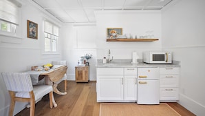 A compact kitchen with white cabinetry, a microwave, a sink, and a wooden dining table with chairs.