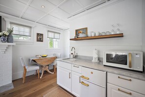 Une cuisine avec des meubles blancs, une table à manger en bois et un micro-ondes encastré.