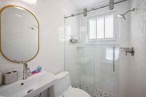 Une salle de bain avec un lavabo blanc, des toilettes et une douche fermée par une paroi de verre.