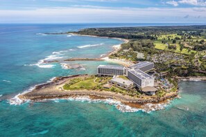 An aerial view of a coastal resort with a large building, a sandy beach, and clear turquoise waters. - Hanau Hideaway, 2026 Remodel, Pool, AC, Turtle Bay (Kahuku)