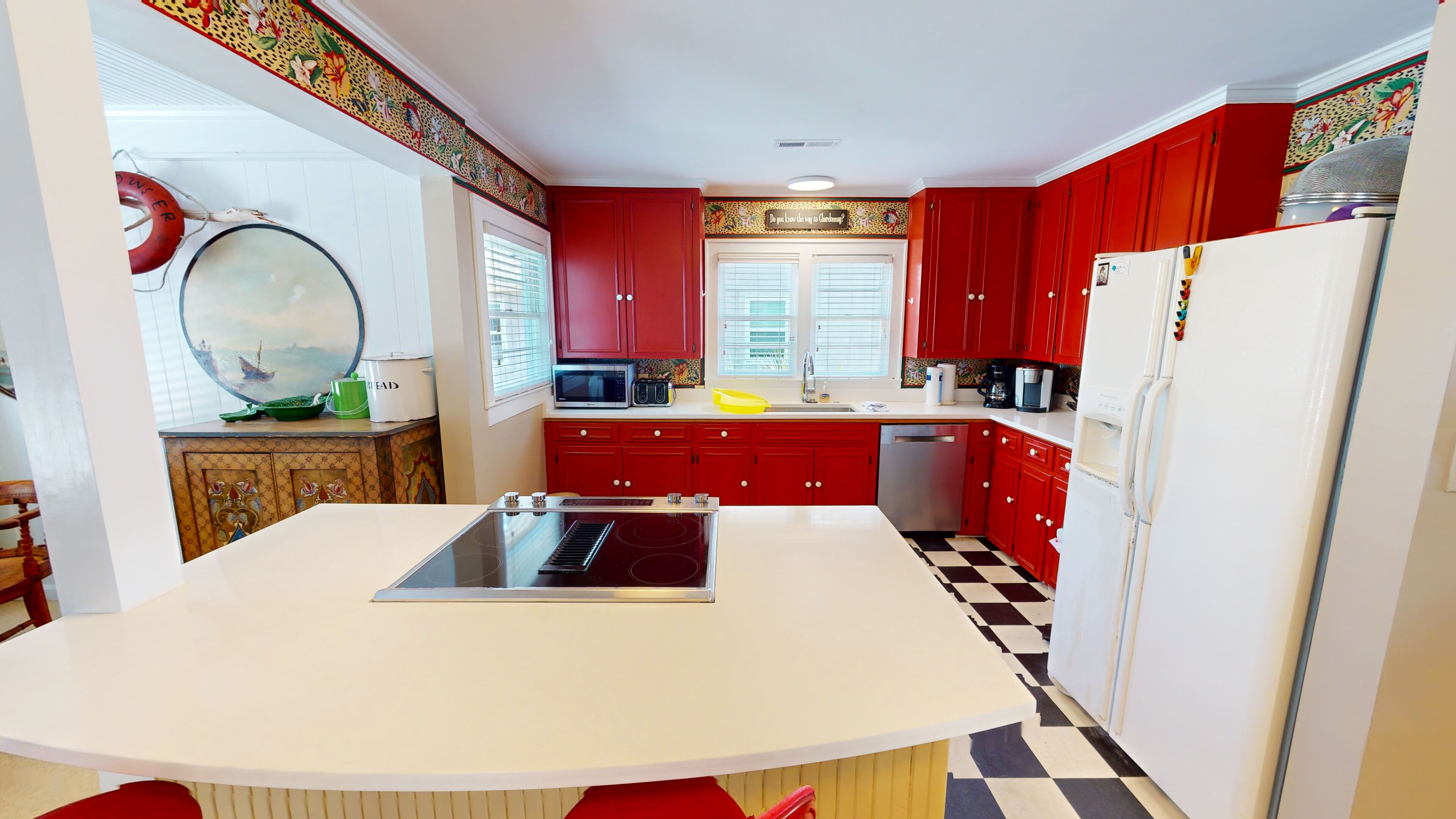 A kitchen with red cabinets, a white countertop, and a black and white checkered floor.