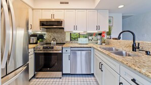 Una cocina moderna con electrodomésticos de acero inoxidable, armarios blancos, encimeras de granito y un lavamanos doble.