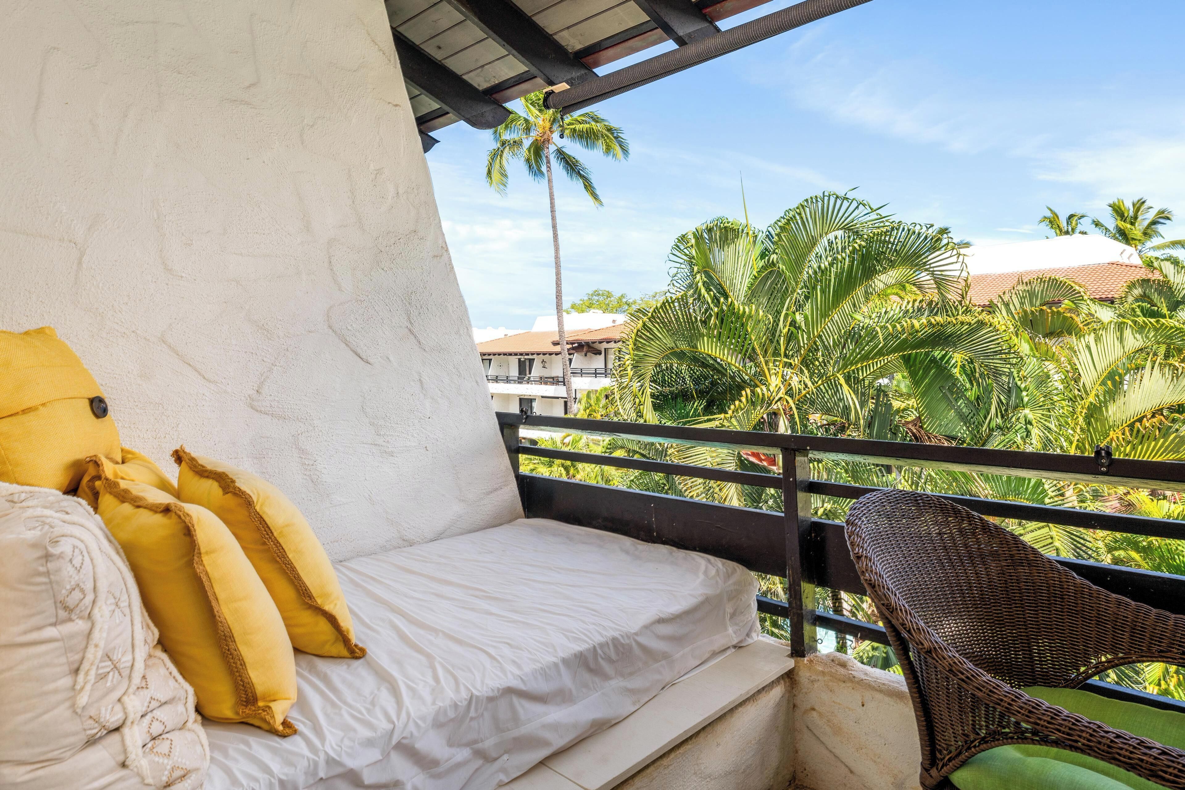 A balcony with a white sofa, yellow pillows, and a wicker chair.