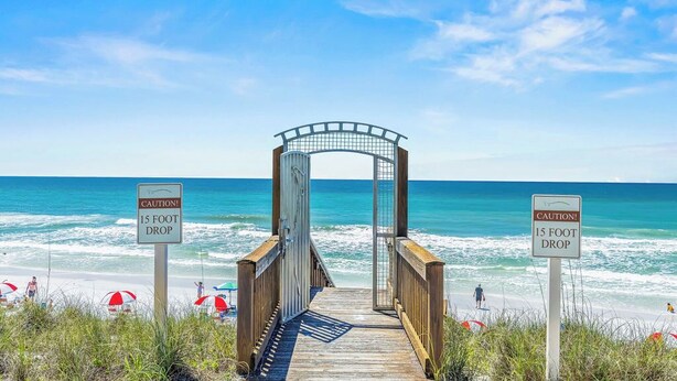 Une promenade en bois mène à une plage, et un panneau d’avertissement indique une falaise d’environ 4,5 mètres de hauteur.