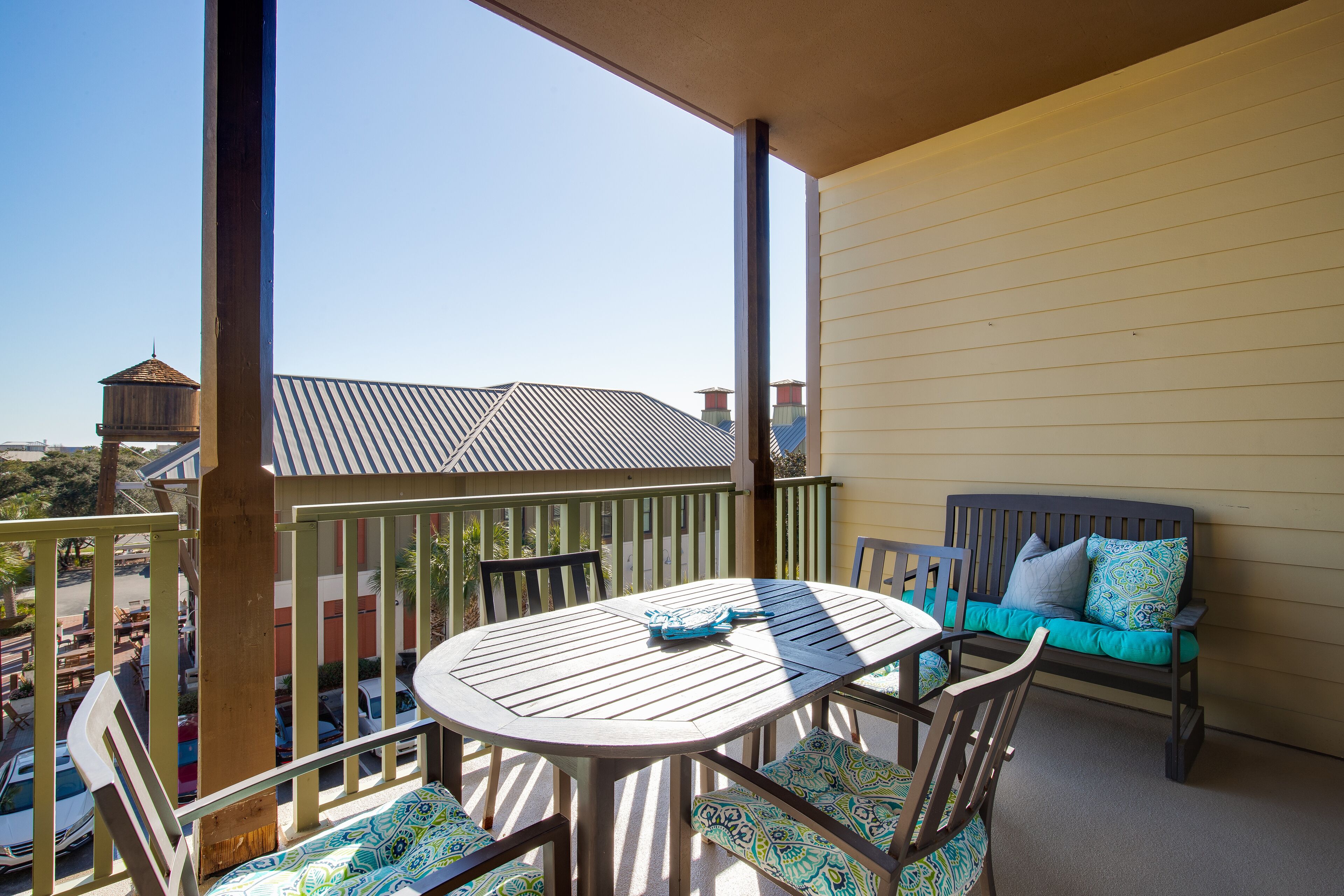 A balcony with a wooden table and chairs, a cushioned bench, and a view of buildings in the background.
