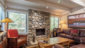 Un salón acogedor con chimenea de piedra, mobiliario de cuero y ventanas amplias.