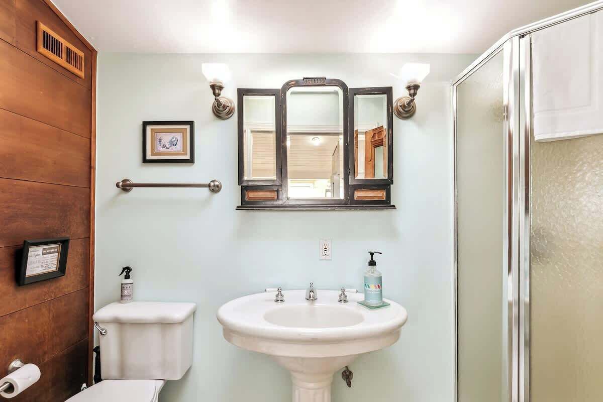 Een badkamer met een wit wastafelmeubel, een spiegel met drievoudig paneel en een douchegedeelte.