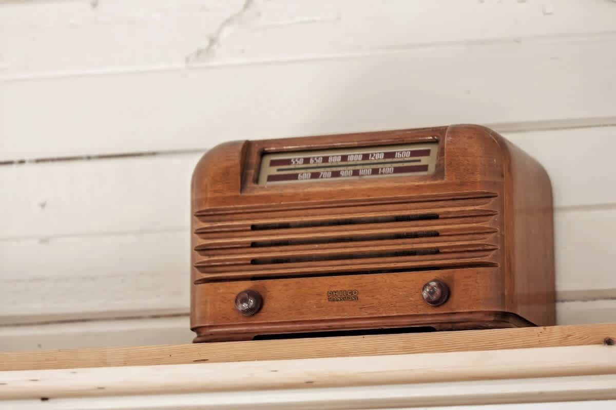A wooden radio with frequency dials and two knobs, placed on a white shelf against a white wall.