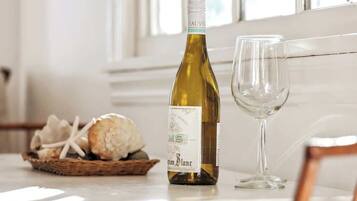 A bottle of white wine and an empty wine glass on a table with a basket of bread and cheese.