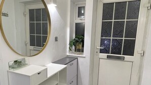 A bathroom with a white vanity, a round mirror, and a door with frosted glass panels. - Newly Refurbished Modern 2 Bedroom Flat (Trimley Saint Mary)