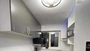 A modern kitchen with a grey countertop, a built-in oven, and a microwave. There are two red chairs and a yellow chair. - Newly Refurbished Modern 2 Bedroom Flat (Trimley Saint Mary)